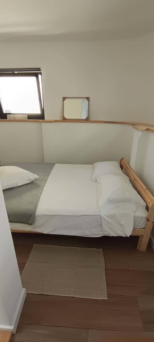 Minimalist bedroom in Pés Verdes Hostel, Ponta Delgada with wooden bed, white linens, skylight, and city view