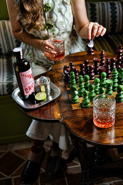 Femme jouant aux échecs avec un verre à La Roquerie, tenant une bouteille de vin et un cocktail