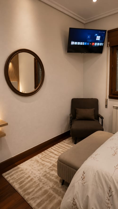 Habitación moderna en Matzuri Nekazalturismoa con televisor mural, espejo redondo, sillón oscuro y cama con vista al mar