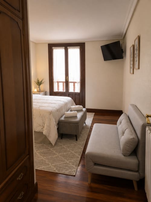 Moderna habitación del hotel MATZURI en Mutriku con cama, sofá, TV de pantalla plana, puertas de balcón y vistas a la montaña