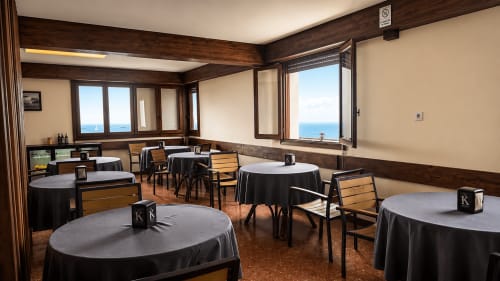 Restaurante de hotel con mesas redondas, vigas de madera y vistas al océano en Mutriku, España