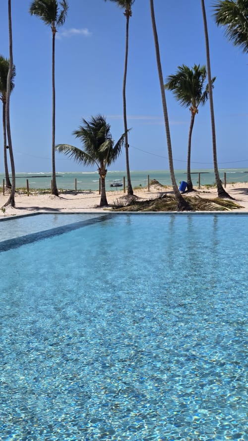 Piscina cristalina com palmeiras e oceano turquesa em Labedi Apartamentos, Porto de Galinhas, Brasil