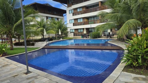 Área da piscina do Labedi Apartamentos em Porto de Galinhas com azulejos azuis, coqueiros e varandas de edifício moderno