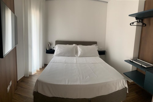 Suite moderna dell'Holiday Suites di Pesaro con letto matrimoniale, lenzuola bianche, pavimentazione in legno e comodini neri.
