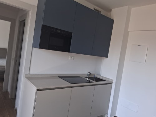 Piccola cucina moderna nella suite di Holiday Suites Pesaro con mobili sospesi scuri, basi chiare, piano cottura e lavello in acciaio inox