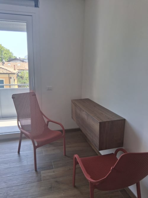 Suite moderna alle Holiday Suites Pesaro con sedie rosse, cassettone in legno e vista sulla città dal balcone