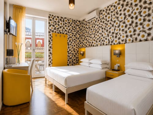 Chambre triple lumineuse avec balcon au B&B Pellicano à Reggio Calabria, papier peint marguerites, lits blancs, accents jaunes
