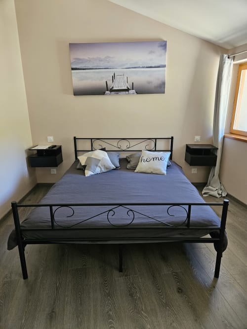 Chambre moderne à l'Auberge Du Campcardos avec lit en métal noir, literie bleue et tableau paisible du lac au-dessus de la tête de lit
