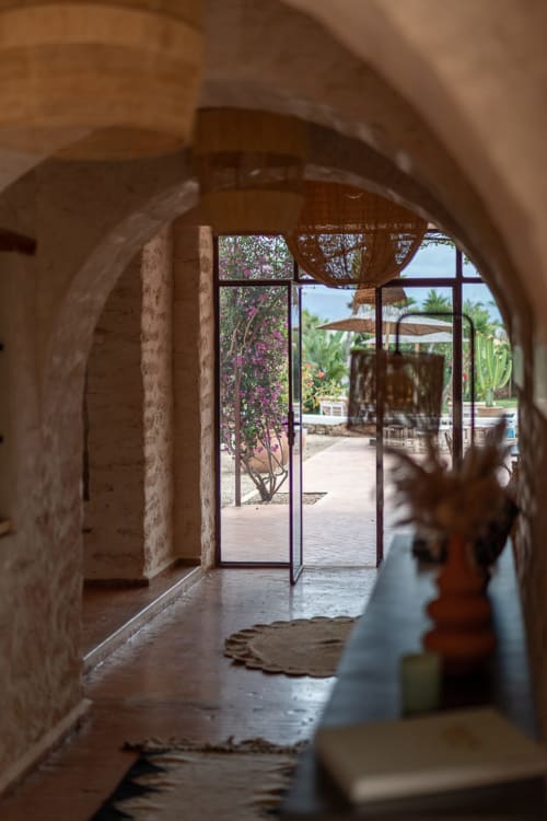 Arched stone corridor at Domaine Belhazar in Essaouira opening to pool area with bougainvillea and parasols