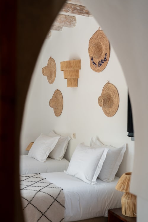 Minimalist bedroom at Domaine Belhazar with woven round wall decor, white bedding, and geometric patterned rug.