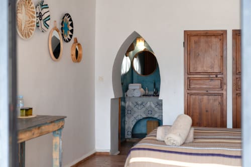 Moroccan-style bedroom at Domaine Belhazar in Essaouira with arched vanity, decorative mirrors, wooden doors, and rolled