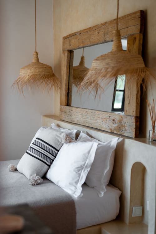 Coastal bedroom at Domaine Belhazar in Essaouira with rustic wooden mirror and woven pendant lights above bed with white