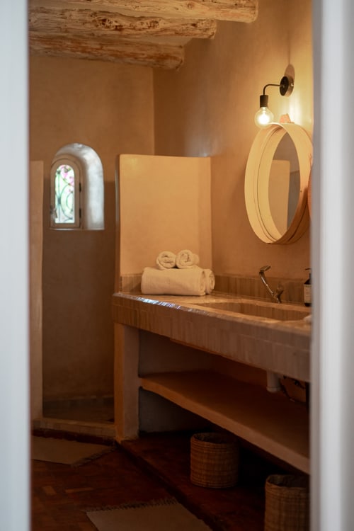 Rustic bathroom at Domaine Belhazar in Essaouira with wooden sink, arched window, and warm lighting