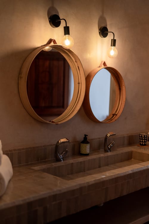 Bathroom vanity at Domaine Belhazar in Essaouira with round wooden mirrors and vintage wall sconces