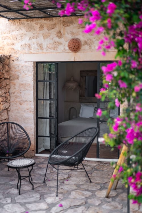 Magenta bougainvillea frames a patio at Domaine Belhazar in Essaouira, with black chair, table, and bedroom view through