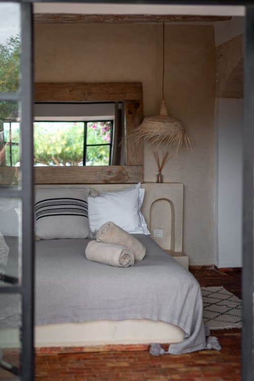 Cozy bedroom at Domaine Belhazar in Essaouira with wooden bed frame, white pillows, and window overlooking garden