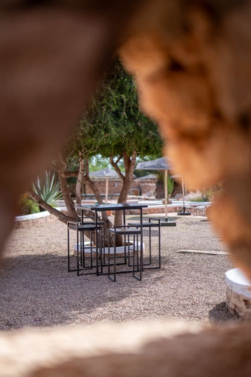 Outdoor dining area at Domaine Belhazar in Essaouira with black table and chairs beneath mature trees on gravel patio