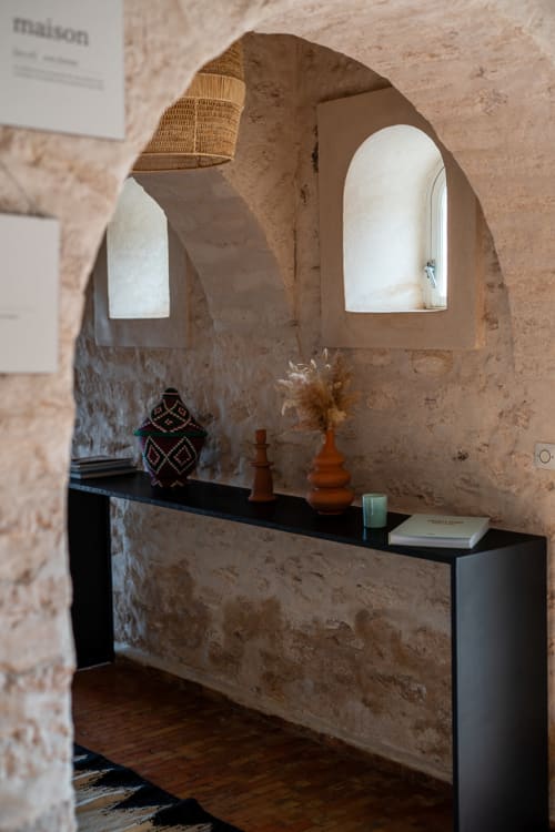 Rustic stone alcove at Domaine Belhazar in Essaouira with arched windows, black console table, and decorative objects
