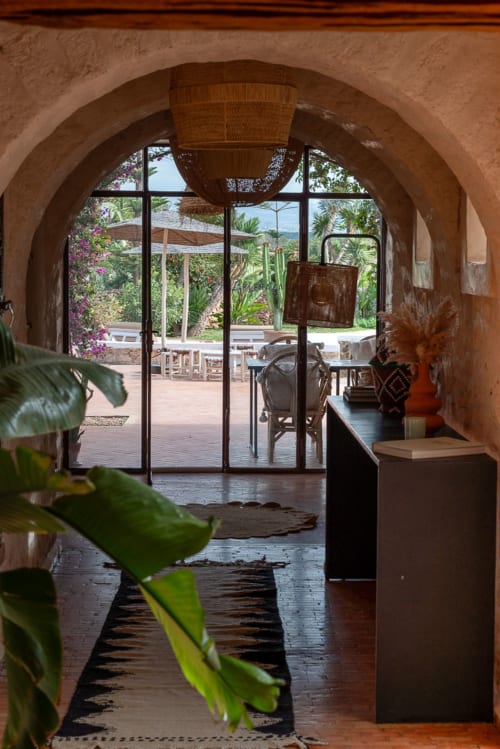 Arched doorway at Domaine Belhazar in Essaouira opening to a Mediterranean garden courtyard with pool area and lounge seating