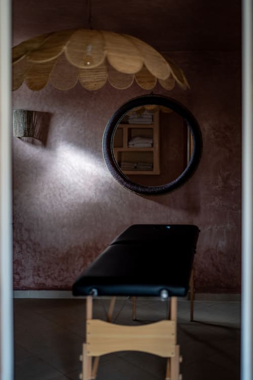 Minimalist bedroom at Domaine Belhazar in Essaouira with black bed, round mirror, and wooden shelf decor