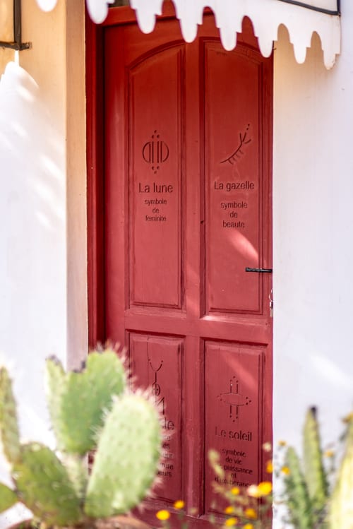 Red decorative door with French symbols at Domaine Belhazar, Essaouira, featuring moon and gazelle motifs with white dripping