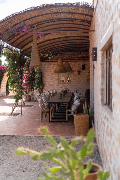 Shaded dining terrace at Domaine Belhazar, Essaouira with woven roof, flowering vines, and wooden furniture