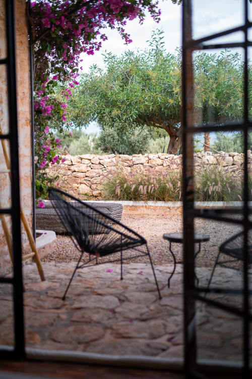 View through French doors to a patio at Domaine Belhazar in Essaouira, with magenta bougainvillea, black chair, and olive