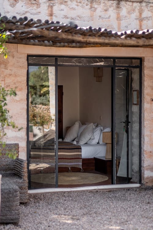 Bedroom interior at Domaine Belhazar in Essaouira with bed, pillows, and black-framed glass doors opening to courtyard