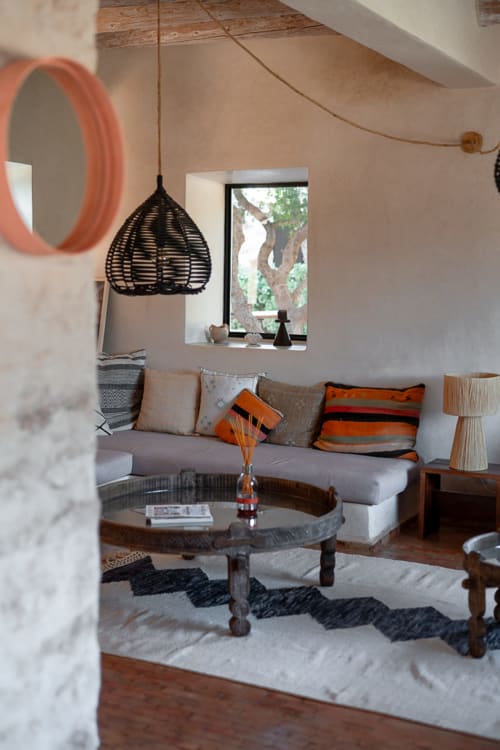 Cozy living room at Domaine Belhazar in Essaouira with gray sofa, woven pendant lamp, and ocean views through window