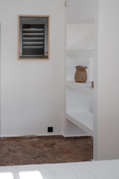 Modern room corner at Domaine Belhazar with white shelving, woven basket, and framed artwork on white walls