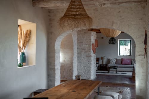 Rustic arched room with wooden table at Domaine Belhazar, Essaouira. Woven pendant light and living area visible beyond.