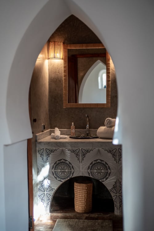 Arched bathroom with wooden mirror, decorative tilework, and rolled towels at Domaine Belhazar, Essaouira