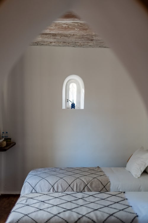 Minimalist bedroom at Domaine Belhazar in Essaouira with arched window, whitewashed walls, and patterned bedding