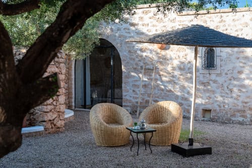 Rustic stone courtyard at Domaine Belhazar, Essaouira with woven lounge chairs under olive tree and dark sail shade