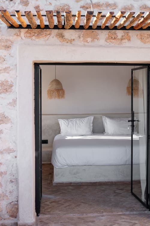 Modern bedroom at Domaine Belhazar in Essaouira with glass doors, white bedding, and woven pendant lights