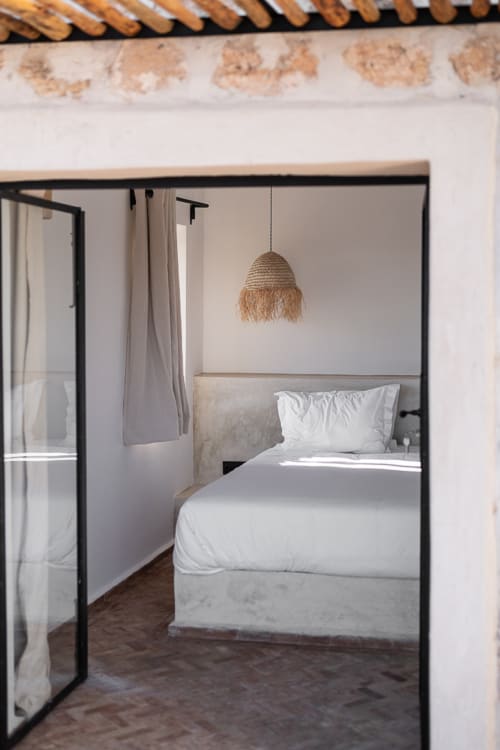 Modern bedroom at Domaine Belhazar in Essaouira with black four-poster bed, white linens, and woven pendant light
