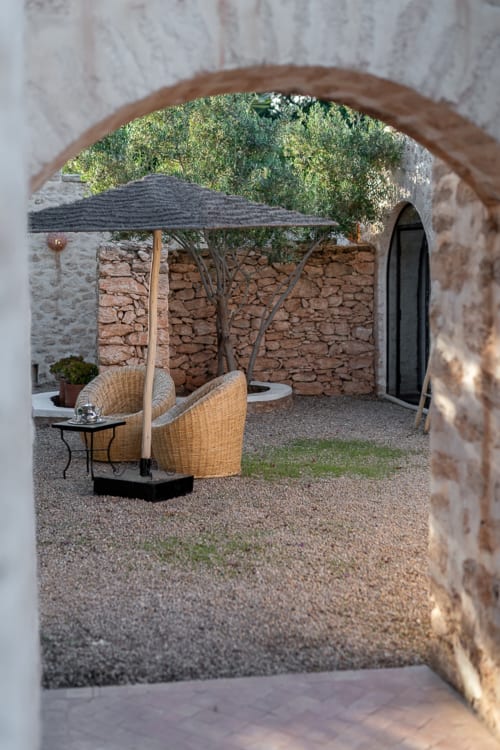 Stone courtyard at Domaine Belhazar, Essaouira with wicker seating, umbrella, and rustic terracotta walls