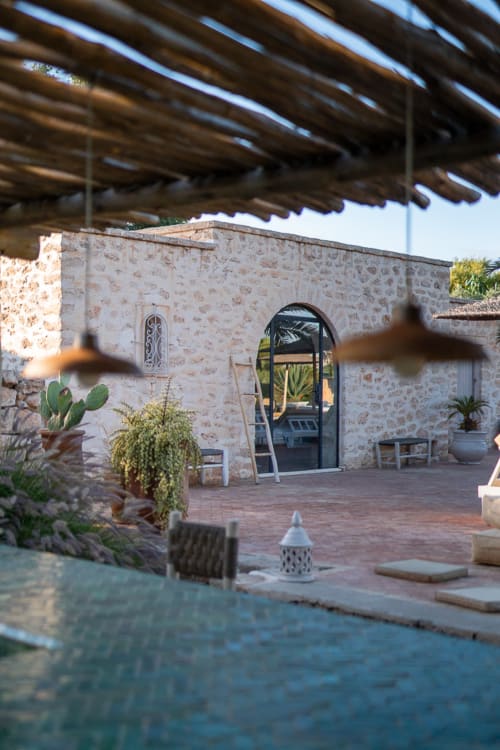 Courtyard entrance of Maison Belhazar in Essaouira with stone walls, arched doorway, potted plants, and wooden pergola