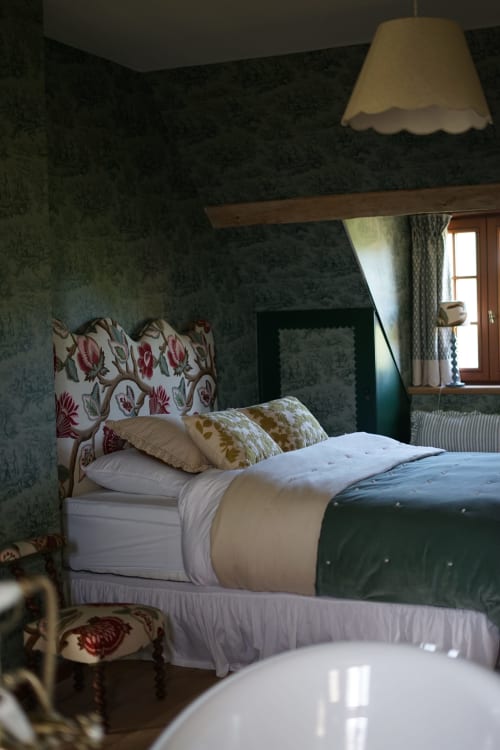 Chambre accueillante avec tête de lit fleurie, papier peint à motifs verts et lampe suspendue à La Roquerie