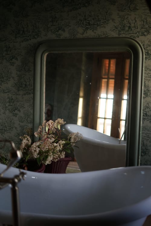Miroir élégant reflétant les fenêtres ensoleillées de la Ferme de La Roquerie avec fleurs blanches et table dressée