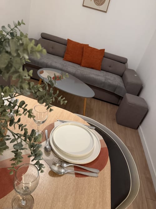 Coin repas d'Appart'NoOm avec couvert de table, décoration en eucalyptus et canapé gris aux coussins orange