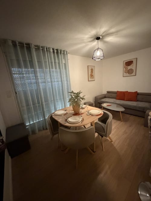 Coin repas moderne avec table ronde, canapé gris, luminaire suspendu et voilages chez Appart'NoOm