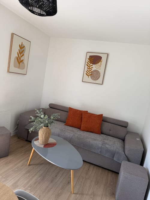 Canapé gris moderne avec coussins orange, art abstrait mural et vase tressé dans le salon de l'appartement Appart'NoOm