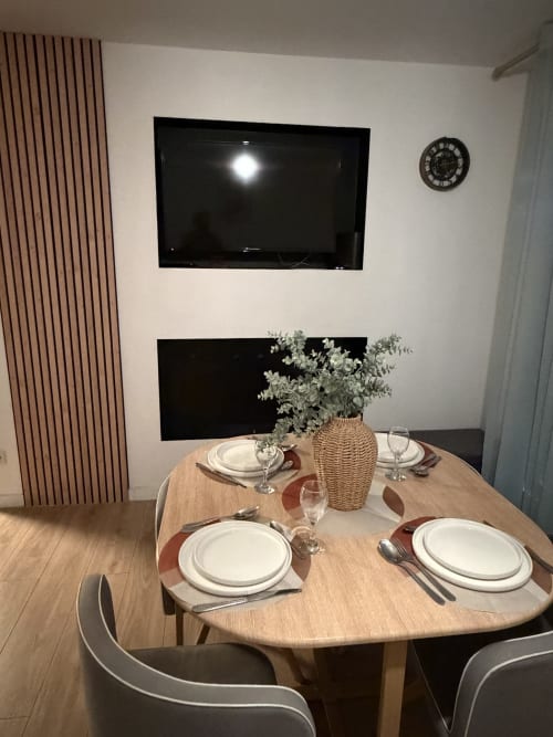 Coin repas à Appart'NoOm avec table dressée, vase tressé, TV murale et décoration contemporaine