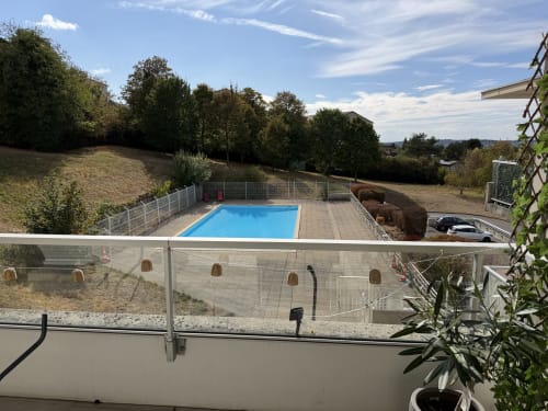 Piscine rectangulaire bleue avec balustrade de terrasse à Appart'NoOm, entourée d'arbres et de paysage champêtre