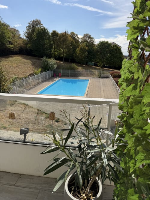 Espace piscine d'Appart'NoOm avec bassin rectangulaire bleu, terrasse et verdure environnante sous ciel dégagé