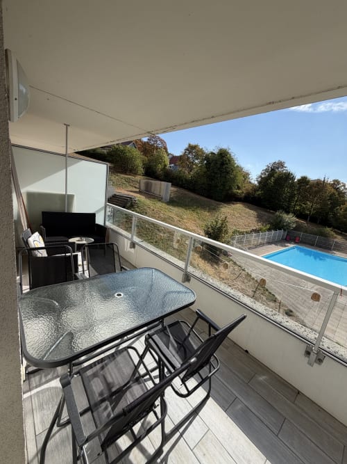 Balcon d'Appart'NoOm avec table à manger, chaises, coin détente et vue sur la piscine donnant sur les jardins