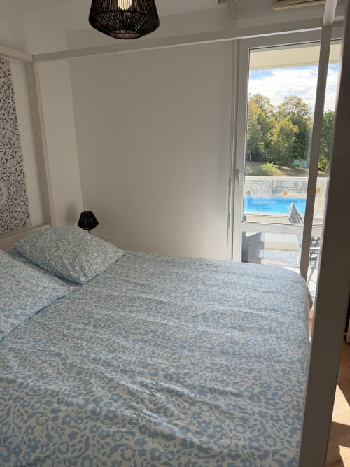 Chambre moderne à Appart'NoOm avec literie à motifs bleus, luminaires suspendus noirs et balcon vue piscine