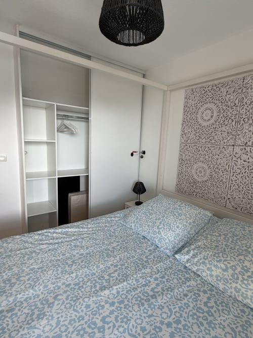 Chambre moderne à Appart'NoOm avec literie bleue à motifs, armoire blanche et décoration murale