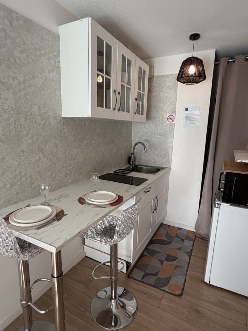 Kitchenette moderne à Appart'NoOm : meubles blancs, plan de travail en marbre, coin repas et luminaires suspendus